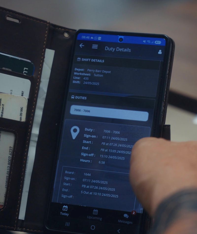 A close-up of a smartphone screen displaying "Duty Details" in a work scheduling app. A finger points to shift information, showing times and locations.